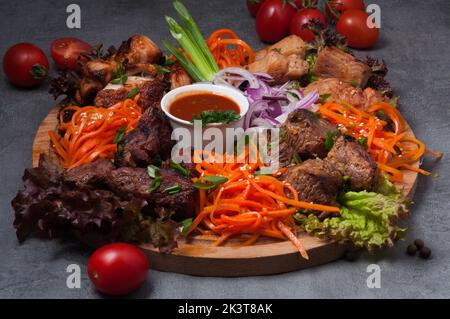 Leckere, gemischte Shish-Kebabs mit Karotten und Tomatensauce auf einem Holzbrett Stockfoto