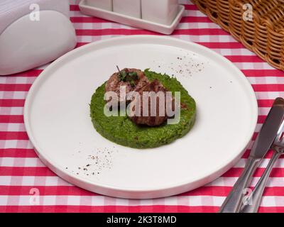 Leckere Kalbsmedaillons auf einem Kissen aus Spinat und getrockneten Tomaten Stockfoto