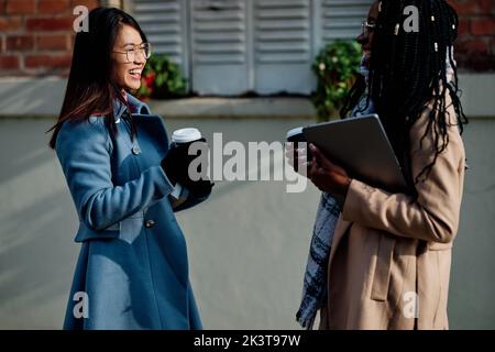 Eine glückliche junge Frau, die ihre Freundin im Café-Garten trifft. Wiedervereinigung, College-Freundschaft. Stockfoto