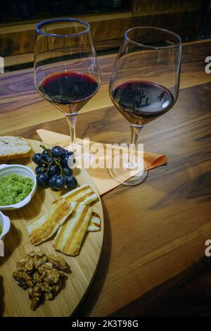 Eine vertikale Nahaufnahme von zwei Gläsern Rotwein und Vorspeisen auf dem Holzhintergrund Stockfoto