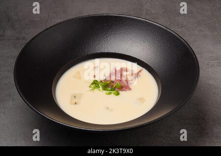 Leckere Käsesuppe mit Speck auf einem schwarzen Teller Stockfoto