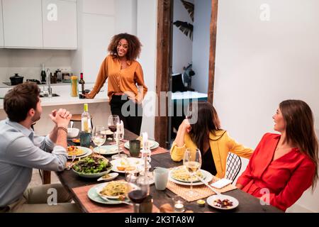 Fröhliche Jugendliche, vielfältige Freunde, die lachen und Spaß am Zeitvertreib haben, während sie sich beim Abendessen zu Hause treffen Stockfoto