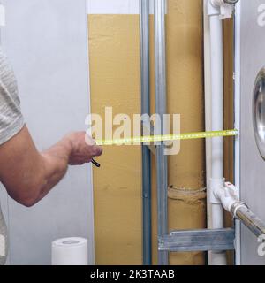 Ein Mann mit einem Maßband misst die Wand für den Wiederaufbau. Mann oder Baumeister mit Maßband Stockfoto