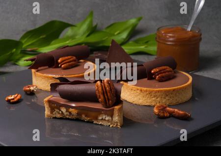 Knuspriges Buttergebäck-Tartlet, gefüllt mit gebratenen Pekannüssen und süßem cremigem Karamell, verziert mit Ganache auf Milchschokolade Stockfoto