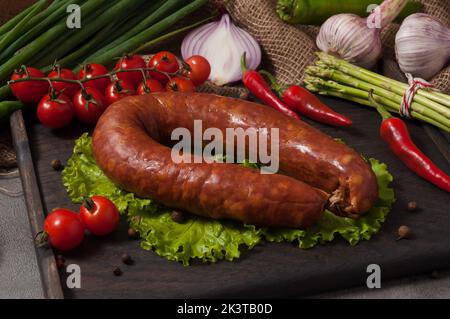 Leckere krakauer Wurst auf einem Holzbrett, dekoriert mit frischem Gemüse Stockfoto