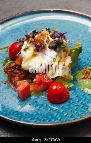 Leckerer Gemüsesalat mit pochiertem Ei und getrockneten Tomaten. Nahaufnahme Stockfoto
