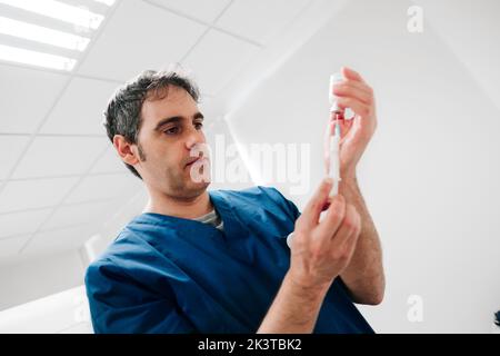 Männlicher Arzt füllt Spritze mit Medizin aus Plastikflasche während der Arbeit in der Klinik Stockfoto