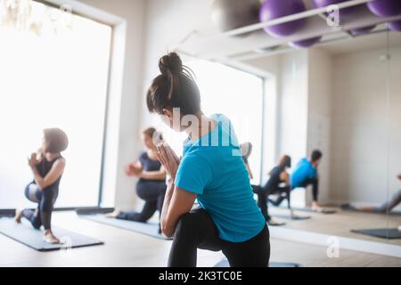 Seitenansicht einer flexiblen weiblichen Yogastrainerin, die zusammen mit einer Gruppe von Menschen im Modder einen drehenden Halbmond-Ausfallschritt auf der Kniepose praktiziert Stockfoto