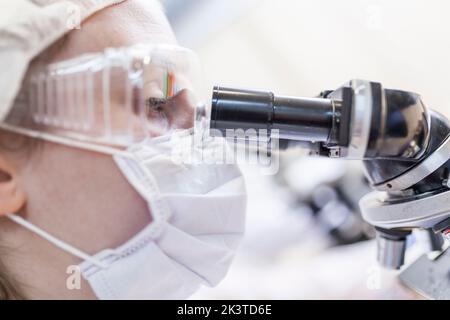 Nahaufnahme einer Wissenschaftlerin, die im Labor durch das Mikroskop schaut Stockfoto
