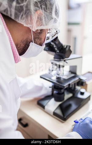 Nahaufnahme von der Seite des Wissenschaftlers, der durch das Mikroskop im Labor schaute Stockfoto