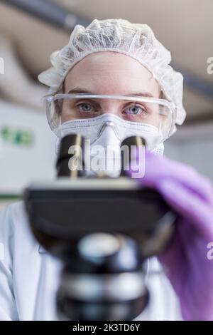 Nahaufnahme der Wissenschaftlerin, die im Labor durch das Mikroskop schaut Stockfoto