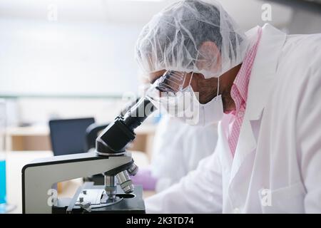 Mann Wissenschaftler Blick durch das Mikroskop im Labor Stockfoto