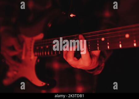 Nahaufnahme eines anonymen Mannes, der in rotem Licht Gitarre spielt Stockfoto