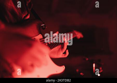 Nahaufnahme eines anonymen Mannes, der in rotem Licht Gitarre spielt Stockfoto