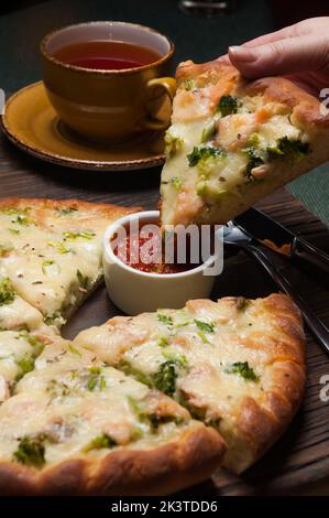 Mädchen taucht eine Scheibe leckere Pizza mit Lachs und Brokkoli in Tomatensauce Stockfoto