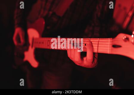 Nahaufnahme eines anonymen Mannes, der in rotem Licht Gitarre spielt Stockfoto