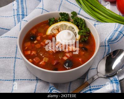 Solyanka ist eine leckere russische Suppe mit verschiedenen Fleisch- und Wurstsorten. Serviert mit saurer Creme und Zitrone Stockfoto