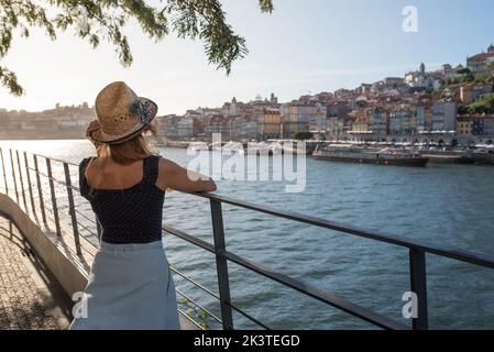 Rückansicht von anonymen weiblichen Touristen, die das wellige Wasser und den städtischen Hafen mit Häusern auf dem Berg von der Brücke in Porto Portugal bewundern Stockfoto