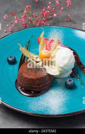 Schmackhafter Fondant mit Eiscreme, verziert mit Beeren und Blumen Stockfoto