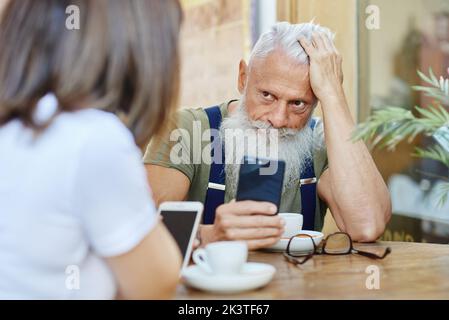 Stilvolle besorgt Dandy Opa browsing auf Smartphone berühren Kopf in der Nähe von beschnitten Frau am Café-Tisch Stockfoto