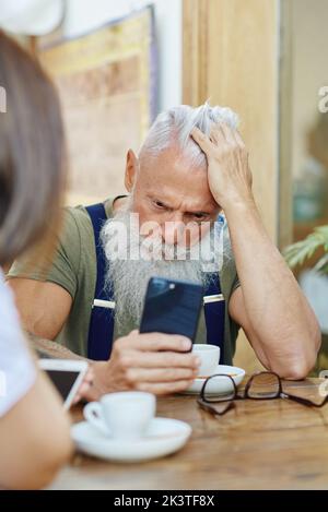 Stilvolle besorgt Dandy Opa browsing auf Smartphone berühren Kopf in der Nähe von beschnitten Frau am Café-Tisch Stockfoto
