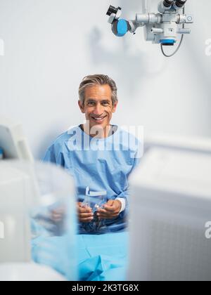 Reifer Mann in medizinischer Uniform lächelt und schaut in die Kamera, während er in einer modernen Klinik arbeitet Stockfoto