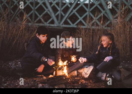 Eine Gruppe junger Freunde, die mit Funkeln auf dem Wald spielen und auf dem Boden sitzen und einander angucken Stockfoto