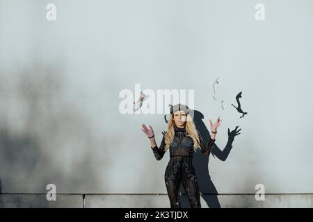 Junge schwarze Frau, die ihre Schuhe neben einer weißen Wand in die Luft wirft und an einem sonnigen Tag in der Stadt einen Hut trägt Stockfoto
