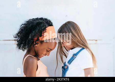 Fröhliche afroamerikanische Mädchen mit besten Freund Spaß in der Nähe der weißen Wand Stockfoto