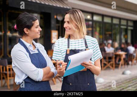 Mitte der Aufnahme von zwei weiblichen Restaurantbesitzern, die eine Liste außerhalb ihres Restaurants überprüfen Stockfoto