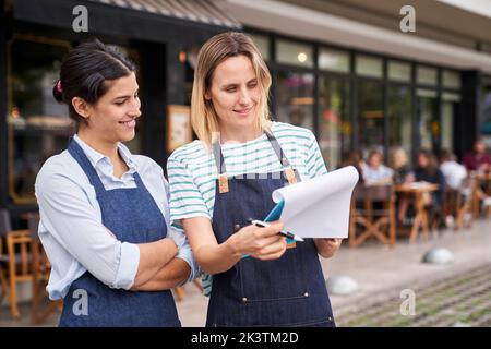 Mitte der Aufnahme von zwei Unternehmerinnen, die eine Liste außerhalb ihres Restaurants überprüfen Stockfoto