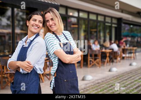 Porträt von zwei glücklichen weiblichen Restaurantbesitzern, die vor ihrem Restaurant posieren und Spaß haben Stockfoto