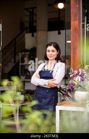 Die Besitzerin der Pflanzenzügnerei lehnte sich mit gekreuzten Armen am Eingang Stockfoto