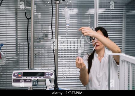Ärztin in weißer Uniform, die Pipette absetzt und den Katheter im Krankenhauszimmer hält Stockfoto