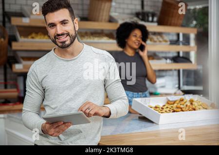 Bäckereibesitzer hält digitale Tablette in der Bäckerei Stockfoto