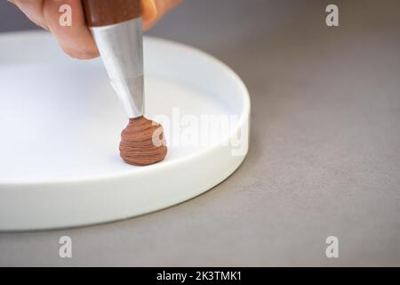 Crop Hand Mann in weißen Chef Jacke Dekoration fancy Gericht mit Zuckerkschokolade aus Paspelsack auf Teller in der Restaurantküche Stockfoto