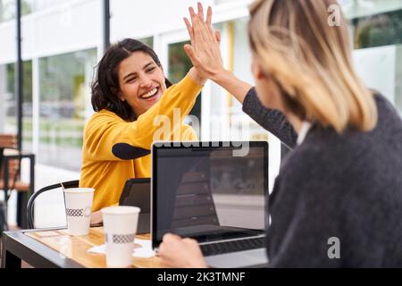 Aufnahme von zwei weiblichen Arbeitskollegen, die sich beim Arbeiten im Freien gegenseitig hoch fiving Stockfoto