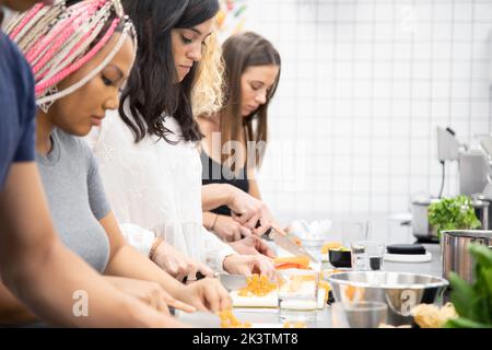 Seitenansicht aufmerksamer, multiethnischer Menschen, die Gemüse mit einem Messer schneiden, während sie in der Küche mit professioneller Ausrüstung zusammenstehen Stockfoto