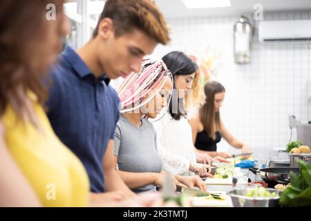 Seitenansicht aufmerksamer, multiethnischer Menschen, die Gemüse mit einem Messer schneiden, während sie in der Küche mit professioneller Ausrüstung zusammenstehen Stockfoto