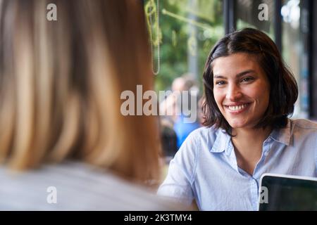 Mittlere Frontansicht der lateinamerikanischen Geschäftsfrau und des Rückens ihrer Kollegin in der Cafeteria des Unternehmens Stockfoto