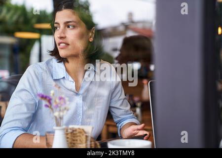 Porträt, das durch das Fenster einer lateinamerikanischen Frau im Café aufgenommen wurde Stockfoto