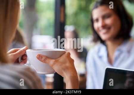 Nahaufnahme von hinten einer Frau, die eine Tasse Kaffee in der Hand hält und mit einem Freund spricht Stockfoto