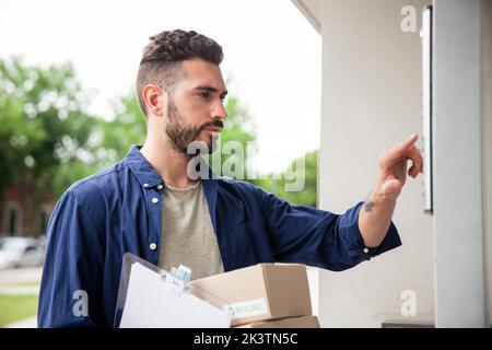 Der Anlieferer stand vor der Tür, während er die Türklingel klingelte Stockfoto