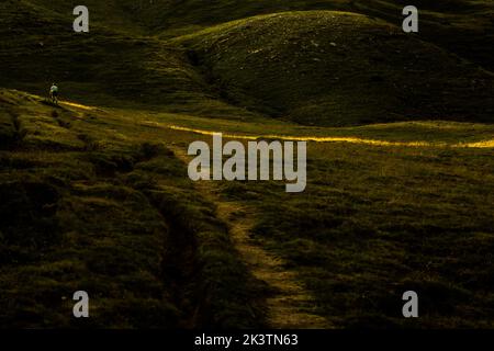 Entfernter nicht erkennbarer Wanderer, der am Sommermorgen durch das grüne, grasbewachsene Hügelland in den Pyrenäen geht Stockfoto