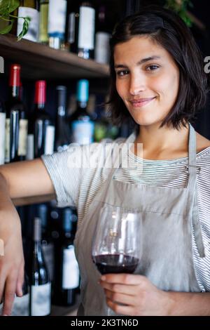 Sommelierin hält ein Glas Wein in der Hand, während sie im Spirituosenladen steht Stockfoto