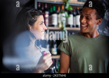 Angestellte im Spirituosengeschäft hält die Flasche, während sie mit dem Kunden spricht Stockfoto