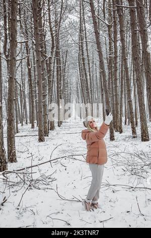 Eine junge Frau steht in einem Kiefernwald und fotografiert die Natur auf ihrem Smartphone. Stockfoto