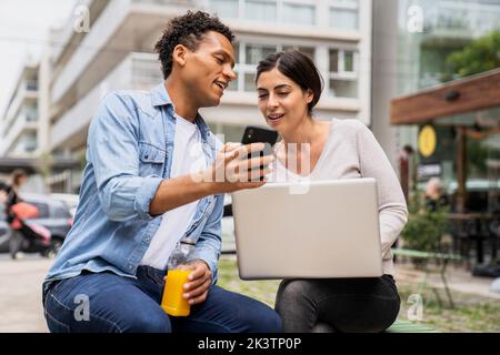 Frontansicht von verschiedenen Paaren, die draußen herumhängen und Spaß mit ihren Smartphones und Computern haben Stockfoto