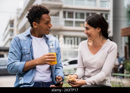 Junger afroamerikanischer Mann und lateinamerikanische Frau, die einen Snack im Freien genießen Stockfoto