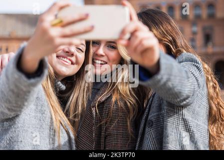 Rückansicht einer Gruppe von nicht erkennbaren Frauen in stilvollem Outfit, die am Wochenende an der Plaza de Espana an einem sonnigen Tag in Sev Selbstschuss auf dem Smartphone gemacht haben Stockfoto